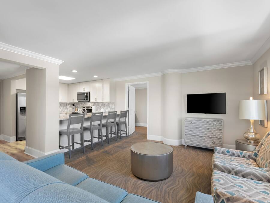 A modern living room with a sofa, a coffee table, a TV, and a kitchen area in the background.