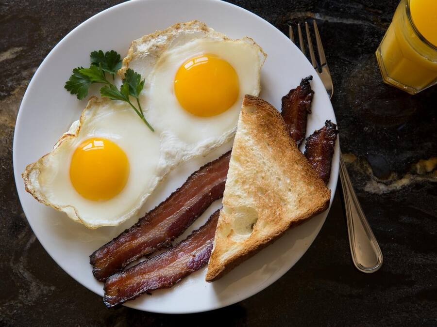 A plate with two fried eggs, bacon, and toast on a marble surface.