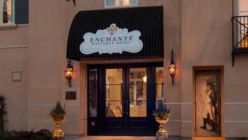 The entrance of the Enchantment Boutique Hotel with a classic facade, a sign above the entrance, and two illuminated lanterns on either side.