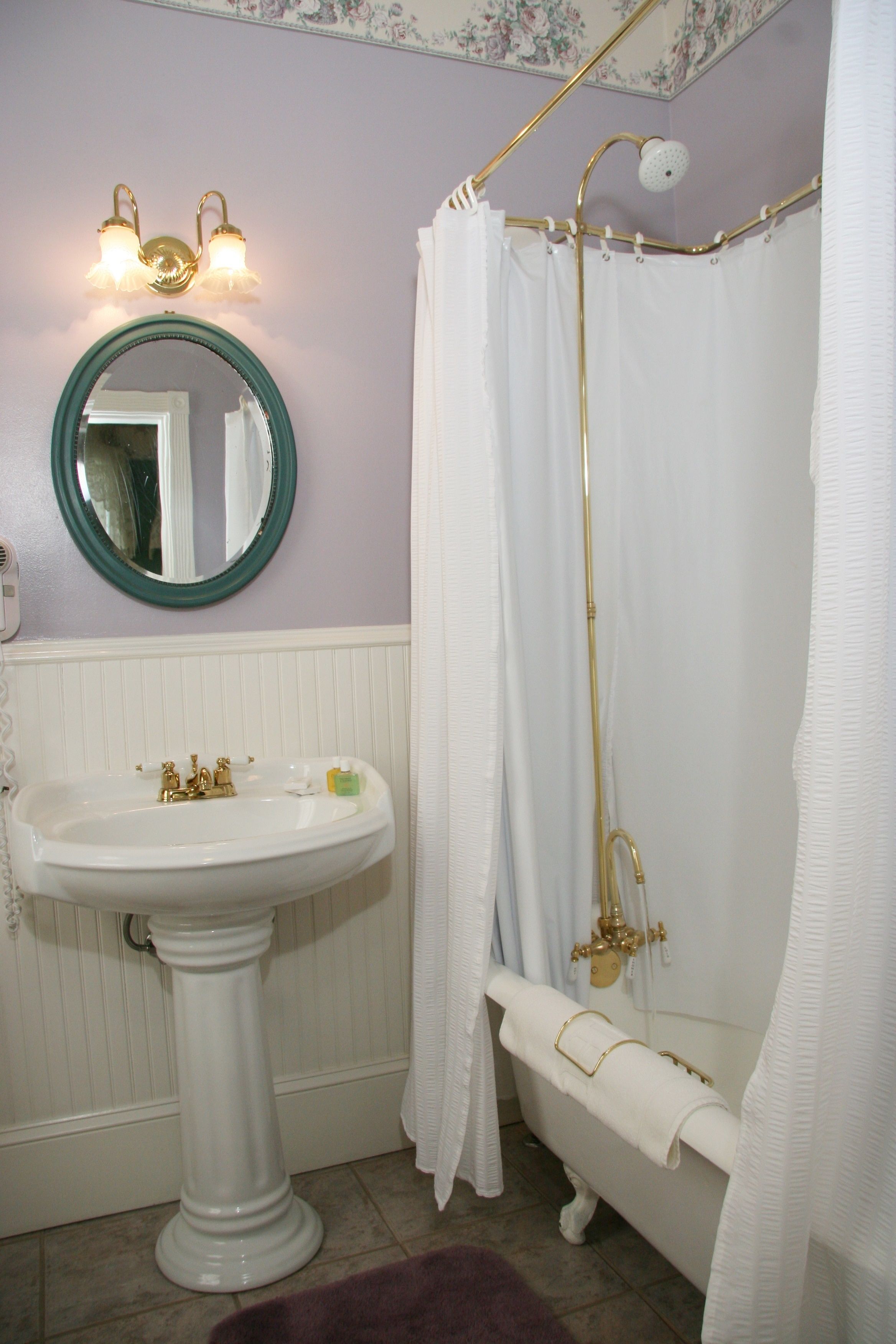 Un baño con lavamanos pedestal, bañera con ducha y espejo con apliques de pared.