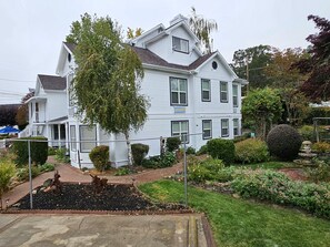 A two-story white house with a large tree in front, surrounded by well-maintained gardens and a small pond.