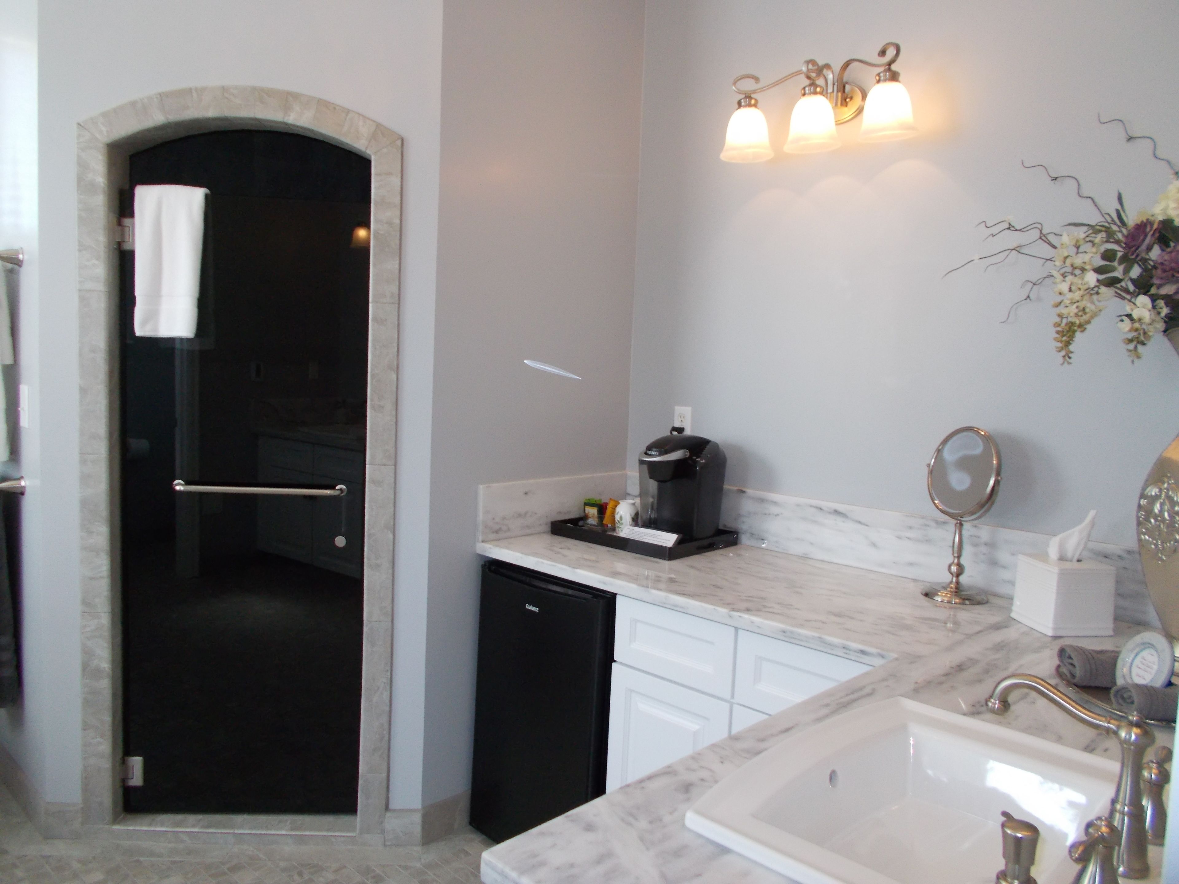 A modern bathroom with a marble sink, a coffee maker, and a shower area.