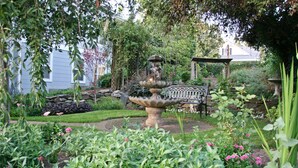 Un jardín con una fuente de piedra, abundante vegetación y un pabellón.