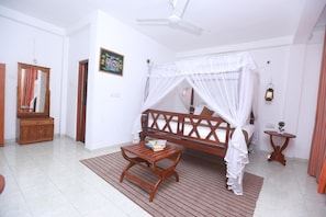 A bedroom with a bed under a canopy, a wooden bench with books, a small table, a mirror, and a ceiling fan. - Palitha Guesthouse Hotel Dandelion  (Unawatuna)