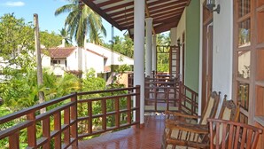 A covered outdoor area with wooden chairs and a table, surrounded by a wooden railing. - Palitha Guesthouse Hotel Dandelion  (Unawatuna)