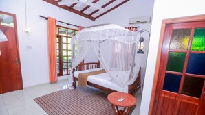 A room with a bed, a small table, a window with curtains, and a door. - Palitha Guesthouse Hotel Dandelion  (Unawatuna)
