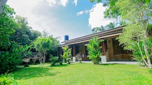 A building with a covered porch, surrounded by lush greenery and a clear sky. - Palitha Guesthouse Hotel Dandelion  (Unawatuna)