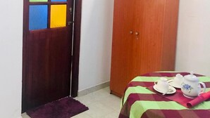 A room with a wooden door with colorful glass panels, a wardrobe, and a bed with a striped bedspread. - Palitha Guesthouse Hotel Dandelion  (Unawatuna)