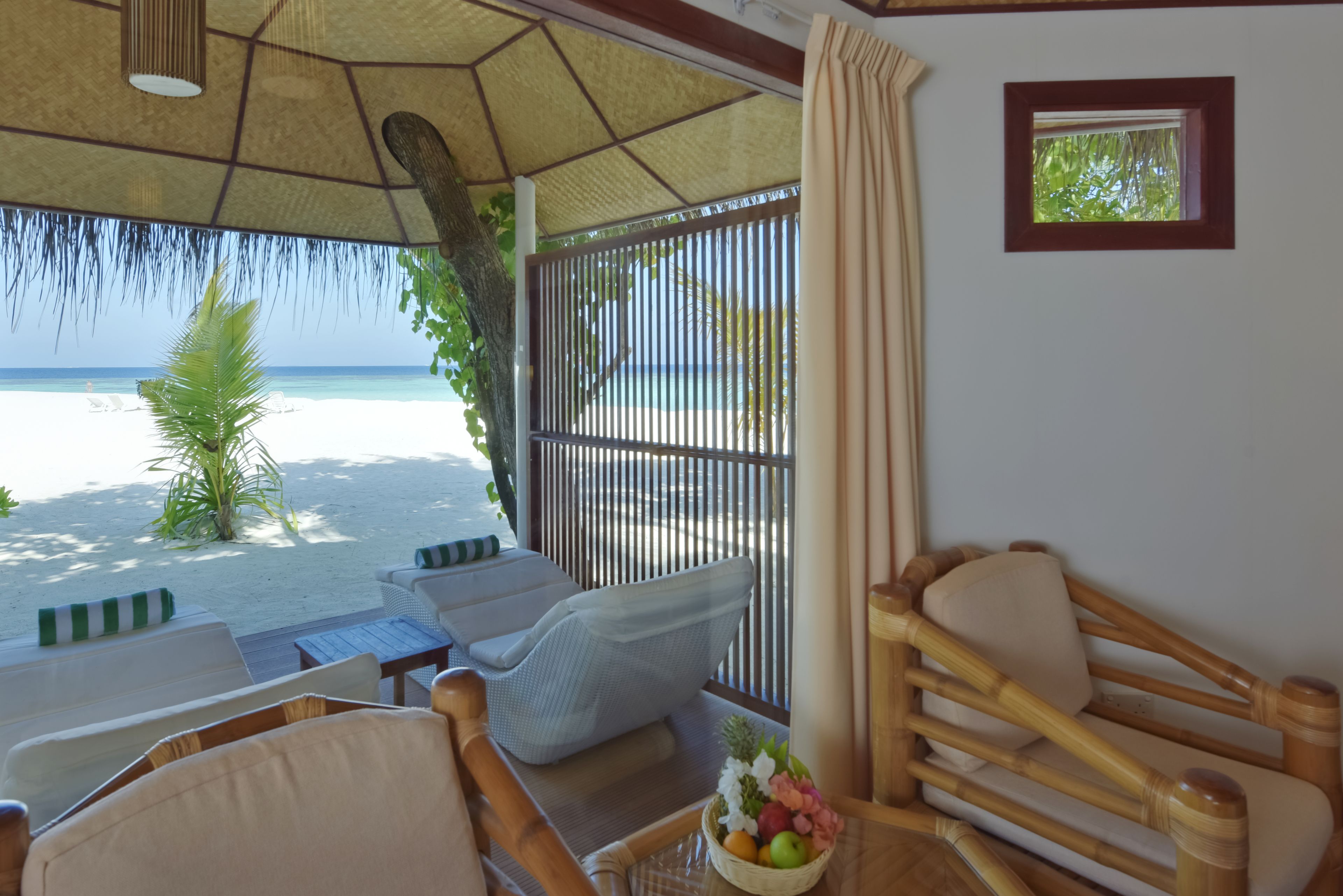 Une chambre située en bord de mer, avec vue sur l’océan, un toit de chaume et une chaise en osier.