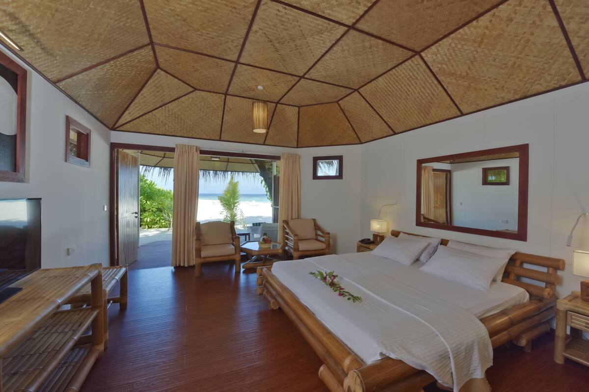 A room with a large bed, wooden furniture, a TV, and a view of the ocean.