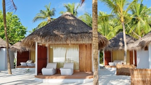 Un resort con cabañas de techo de paja, asientos blancos acolchados y palmeras.