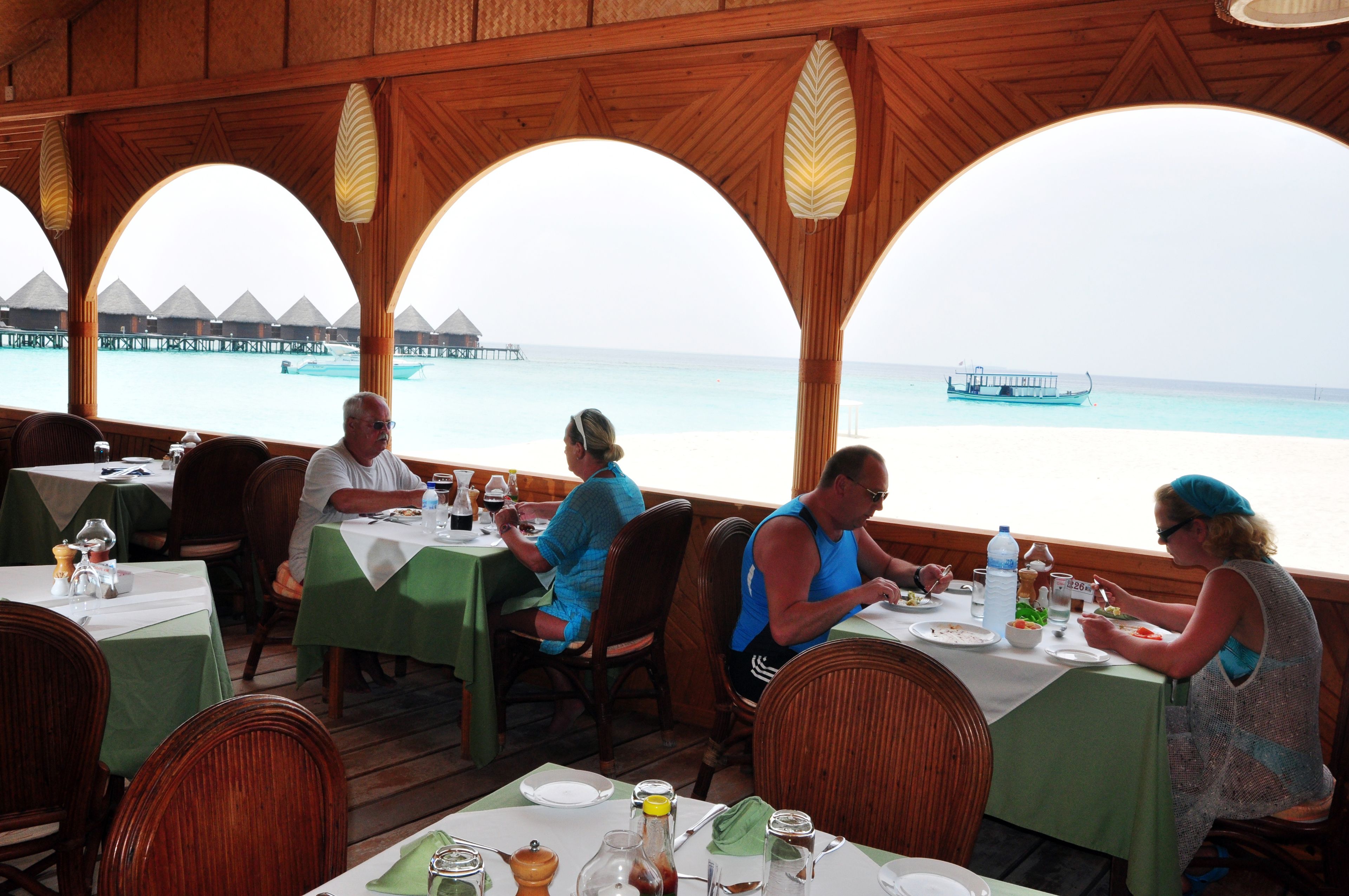 Een restaurant met houten architectuur en grote ramen met uitzicht op een strand.