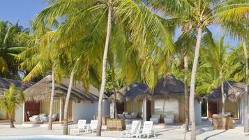 A poolside area with palm trees, thatched-roof huts, and lounge chairs.
