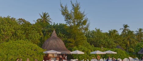 Un restaurante frente a la playa con terraza y estructuras de techo de paja.