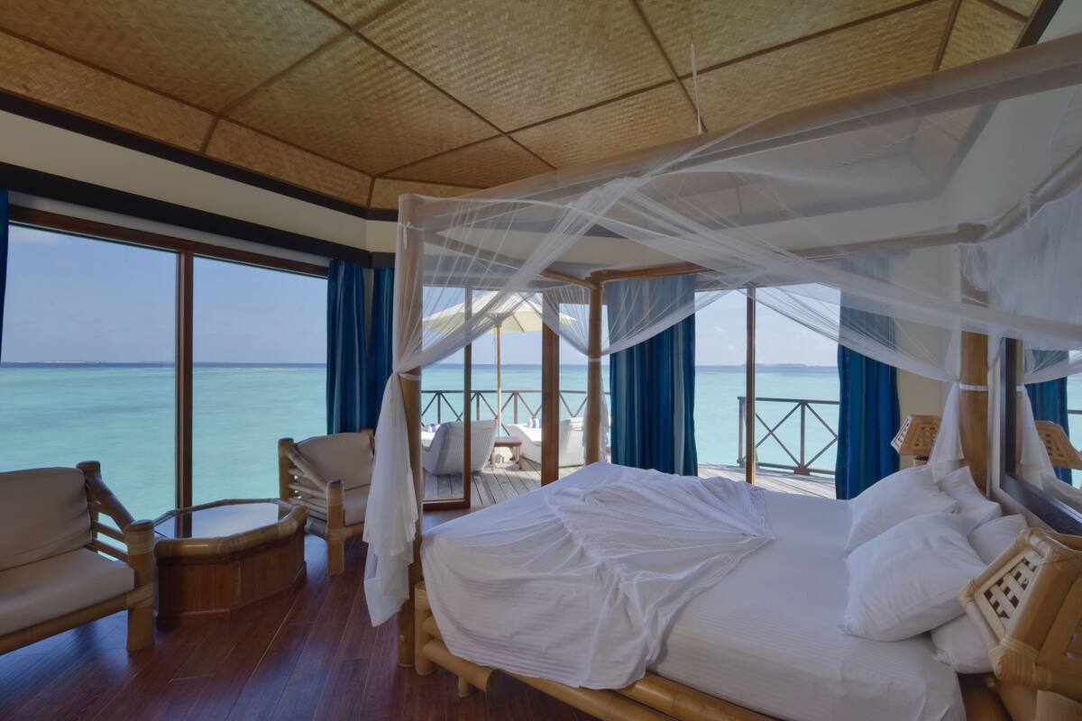 A room with a bed under a canopy, wooden furniture, and a view of the sea.