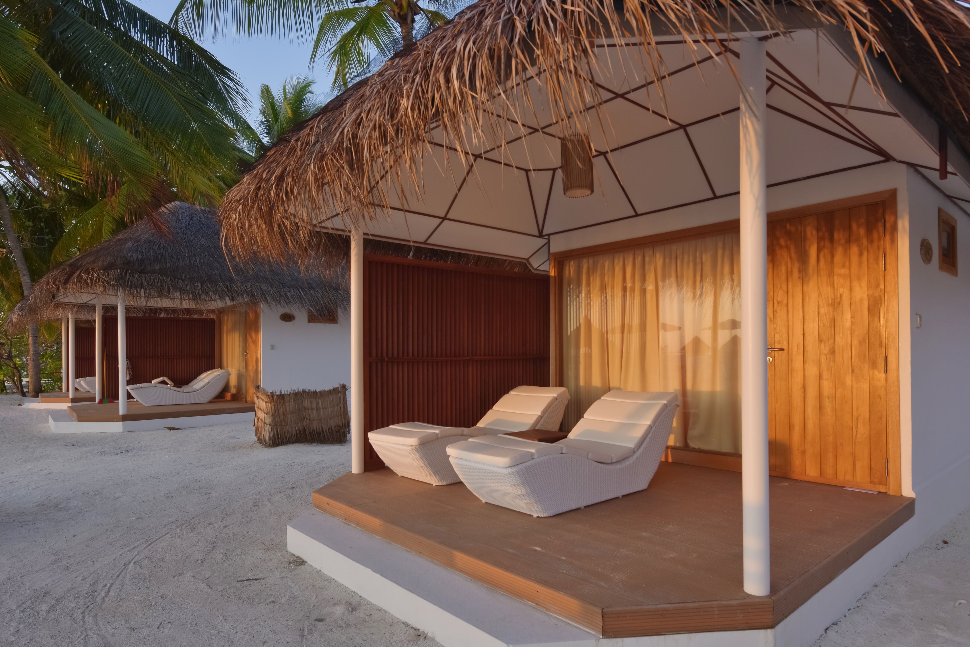 A beachside resort with a thatched-roof structure, two lounge chairs, and a wooden deck.