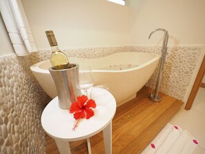 A bathroom with a freestanding bathtub, a small table with a bottle and a glass, and a red flower. - Myra Seafront Suites with Lov (Cap Malheureux)