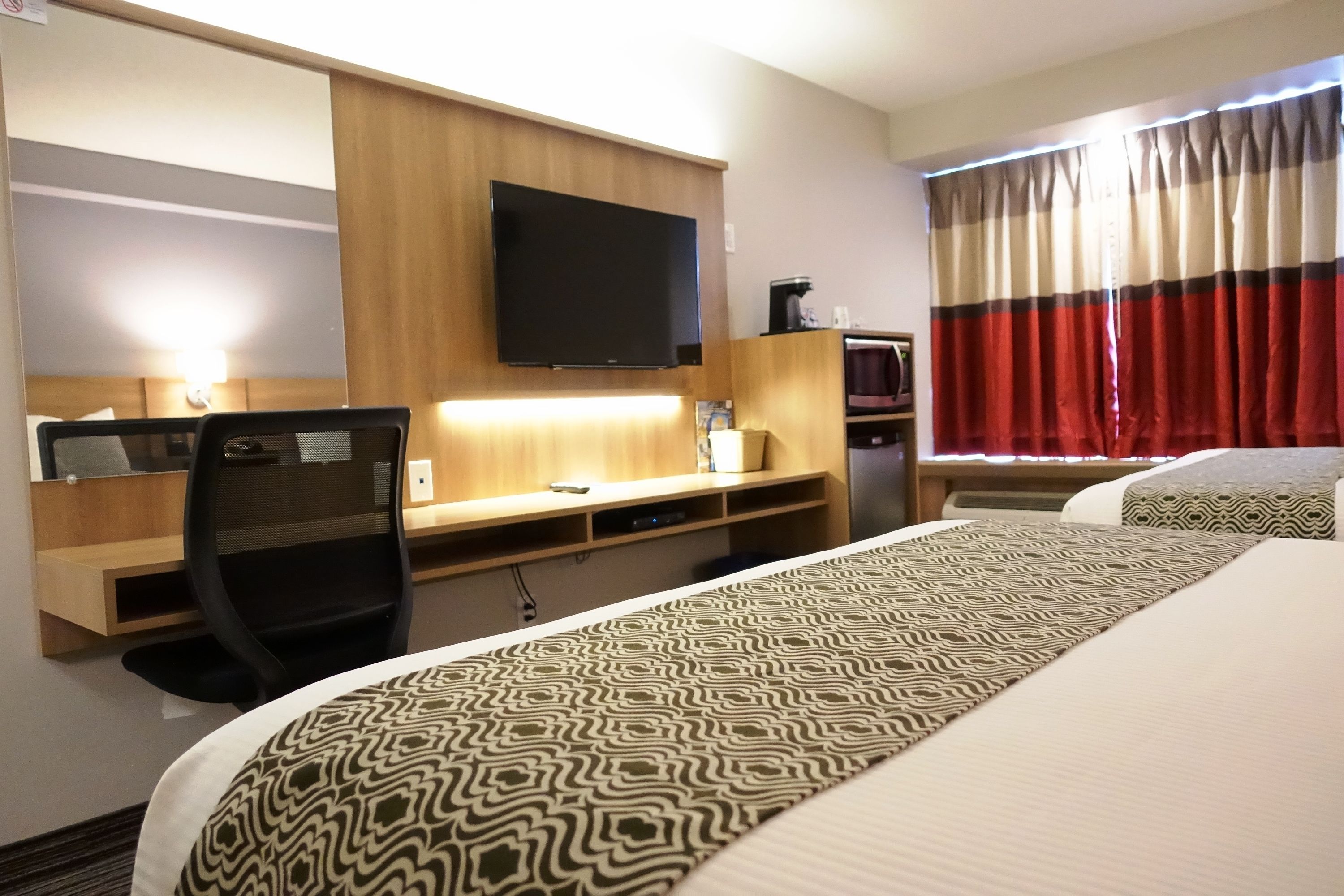 Habitació d'hotel amb llit, escriptori amb cadira, televisió de pantalla plana i cafetera.
