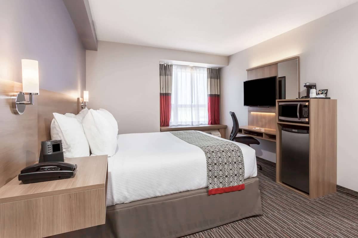 A hotel room with a bed, bedside table, TV, microwave, and a small desk area.