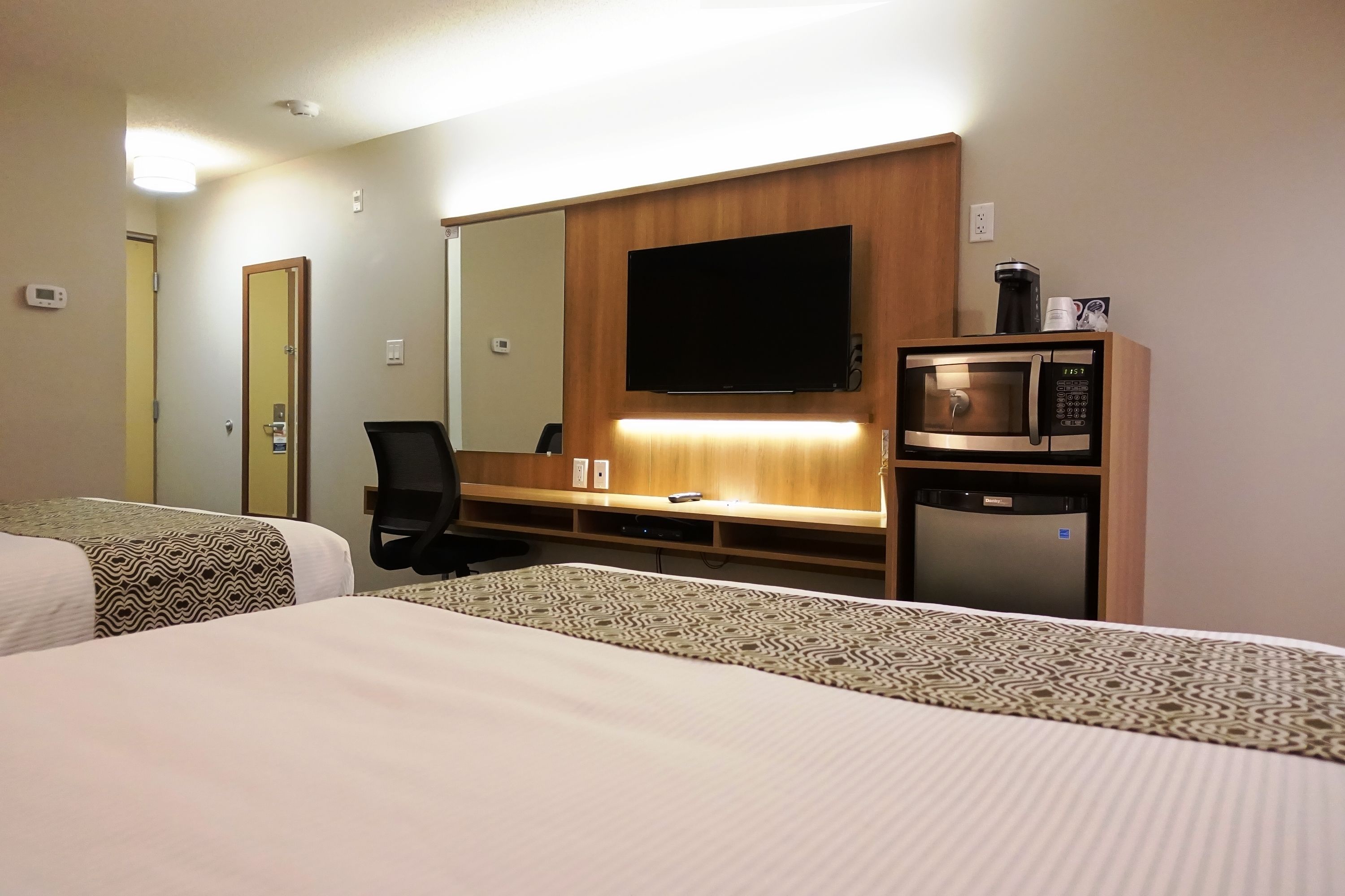 Habitación de hotel con dos camas, un escritorio con silla, televisión, microondas y cafetera.