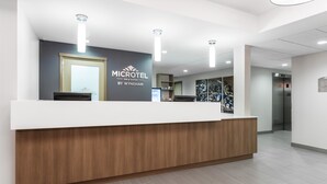 A reception desk with a white counter and wooden base, overhead lighting, and a sign for 'MICROTEL INN & SUITES BY WYNDHAM'. - Microtel by Wyndham Casselman (Casselman)