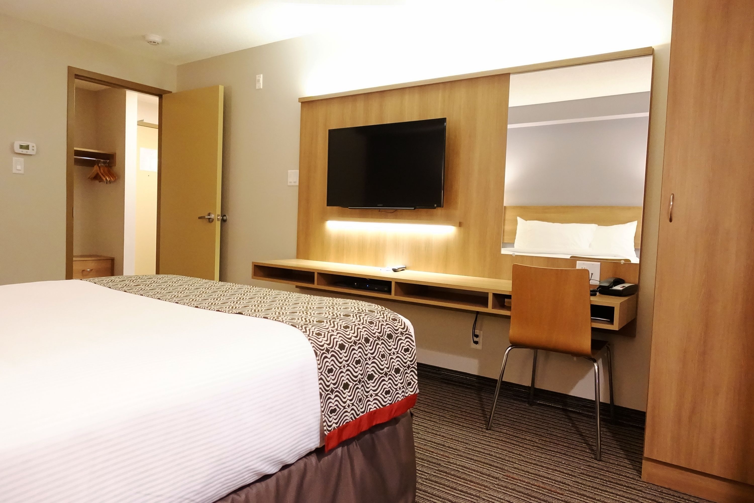 Una habitación de hotel con una cama grande, un escritorio con silla, un televisor montado en la pared y un armario.