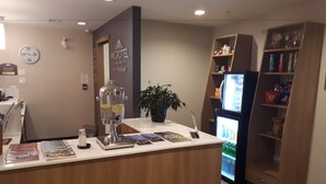 A reception desk with a glass dispenser, magazines, a clock, and a refrigerator stocked with beverages. - Microtel by Wyndham Casselman (Casselman)