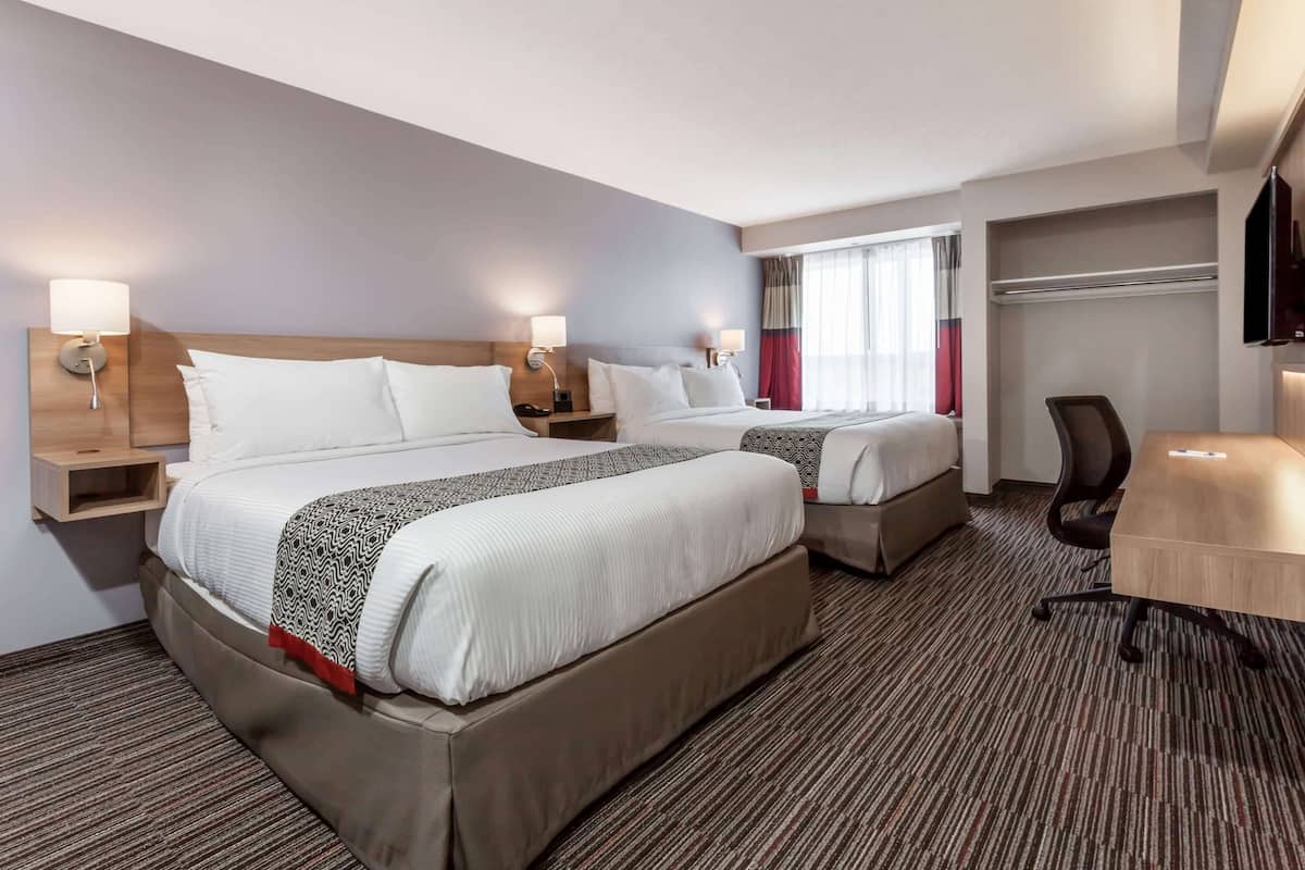A hotel room with two beds, a desk, a chair, and a TV.
