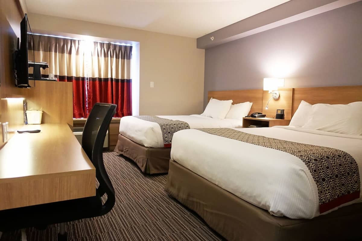 A hotel room with two beds, a desk, a chair, a TV, and a bedside table with a lamp.