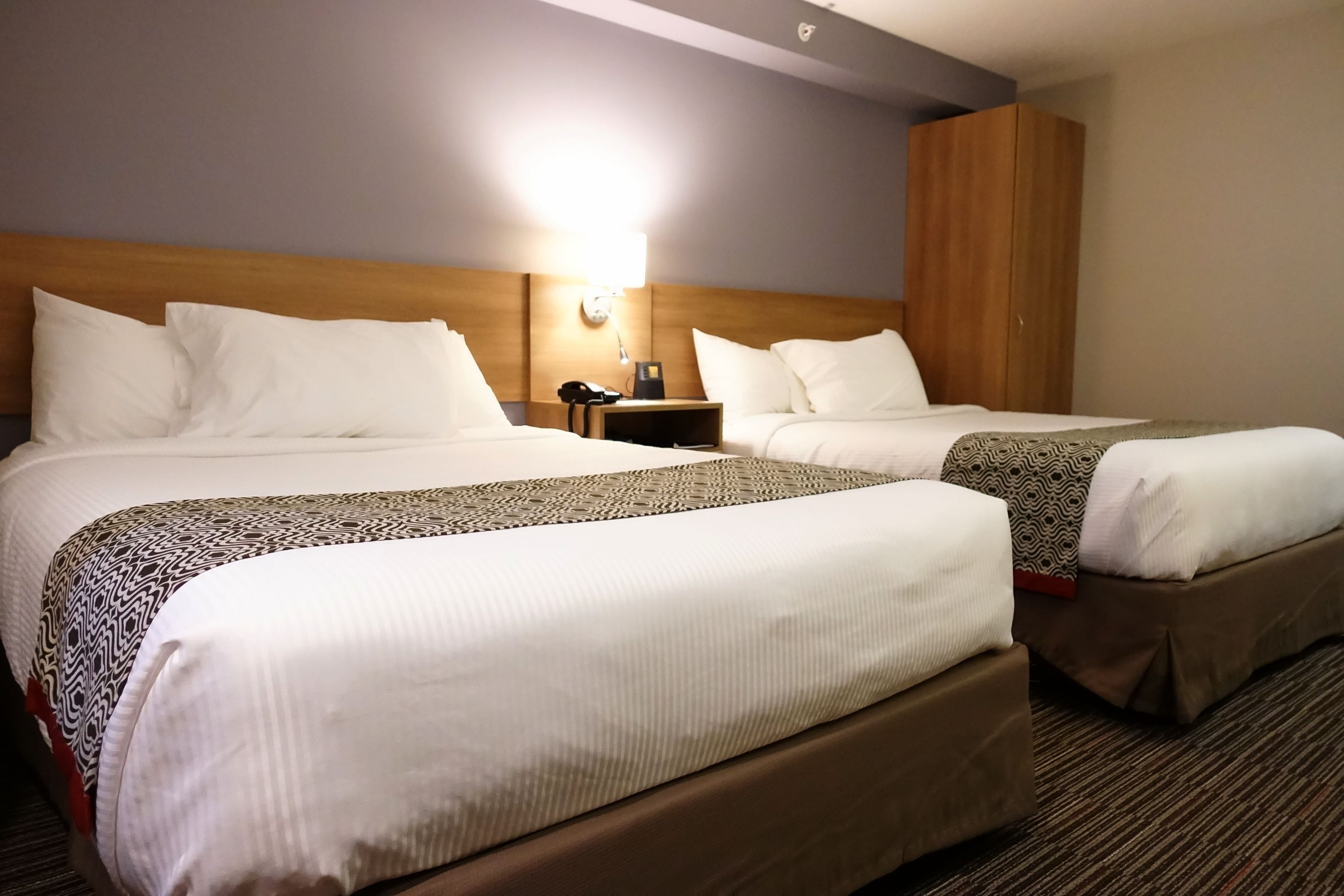 A hotel room with two beds, a nightstand with a lamp, and a wardrobe.