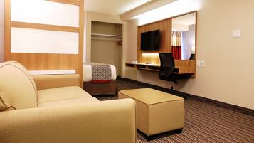 Quarto de hotel com cama, sofá, escrivaninha com cadeira, espelho e televisão.