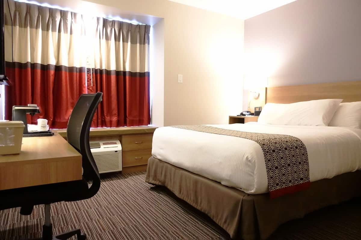 A hotel room with a bed, desk, chair, and a window with curtains.