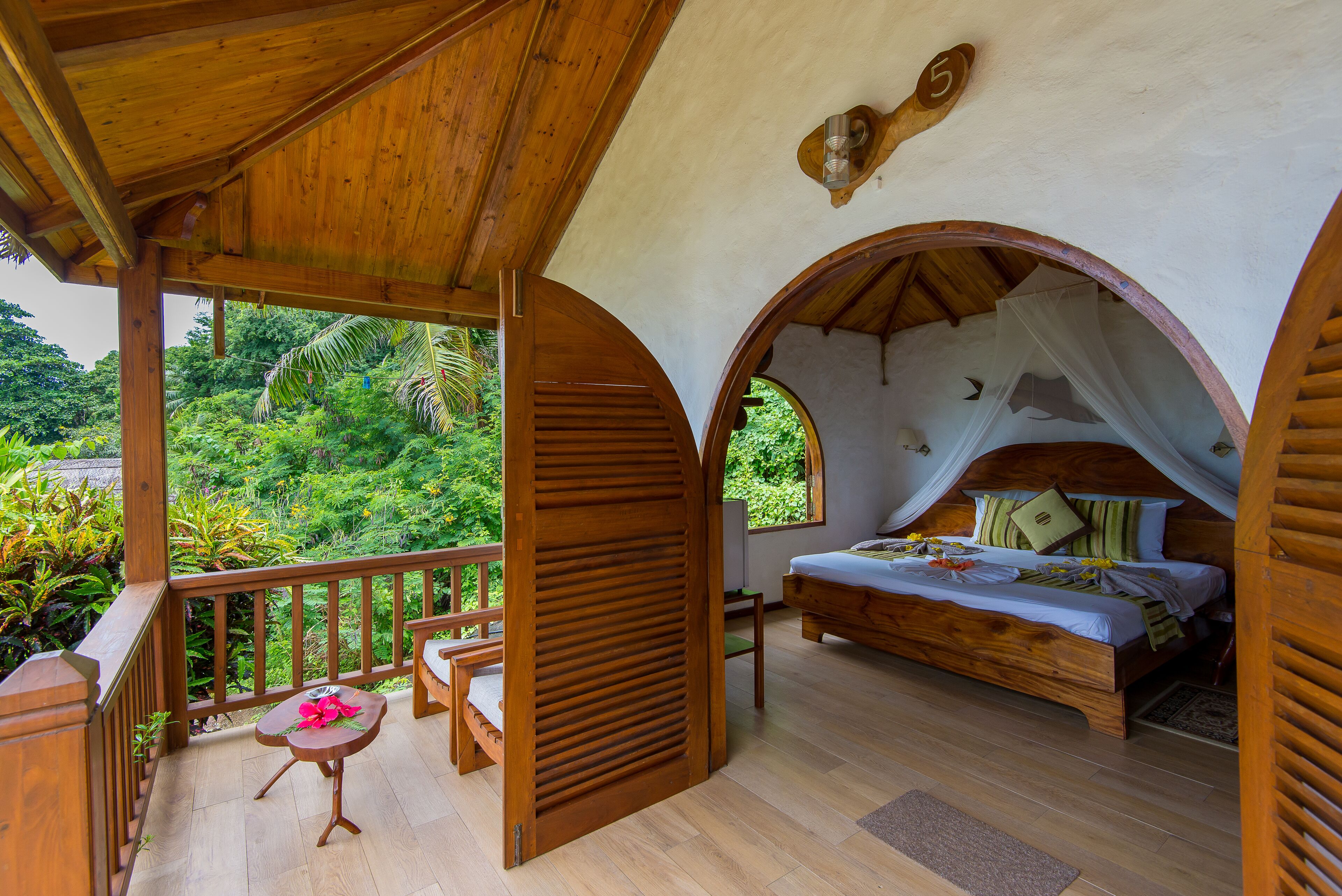 Un dormitorio con cama de madera, un balcón con baranda de madera y vistas a exuberante follaje.