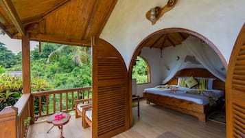 Un dormitorio con cama de madera, un balcón con baranda de madera y vistas a exuberante follaje.