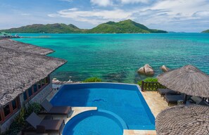 A poolside area with a clear view of the ocean and a mountainous landscape in the background. - Colibri Guest House (Praslin Island)
