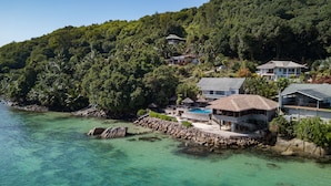 A coastal property with a swimming pool, multiple buildings, and lush greenery. - Colibri Guest House (Praslin Island)