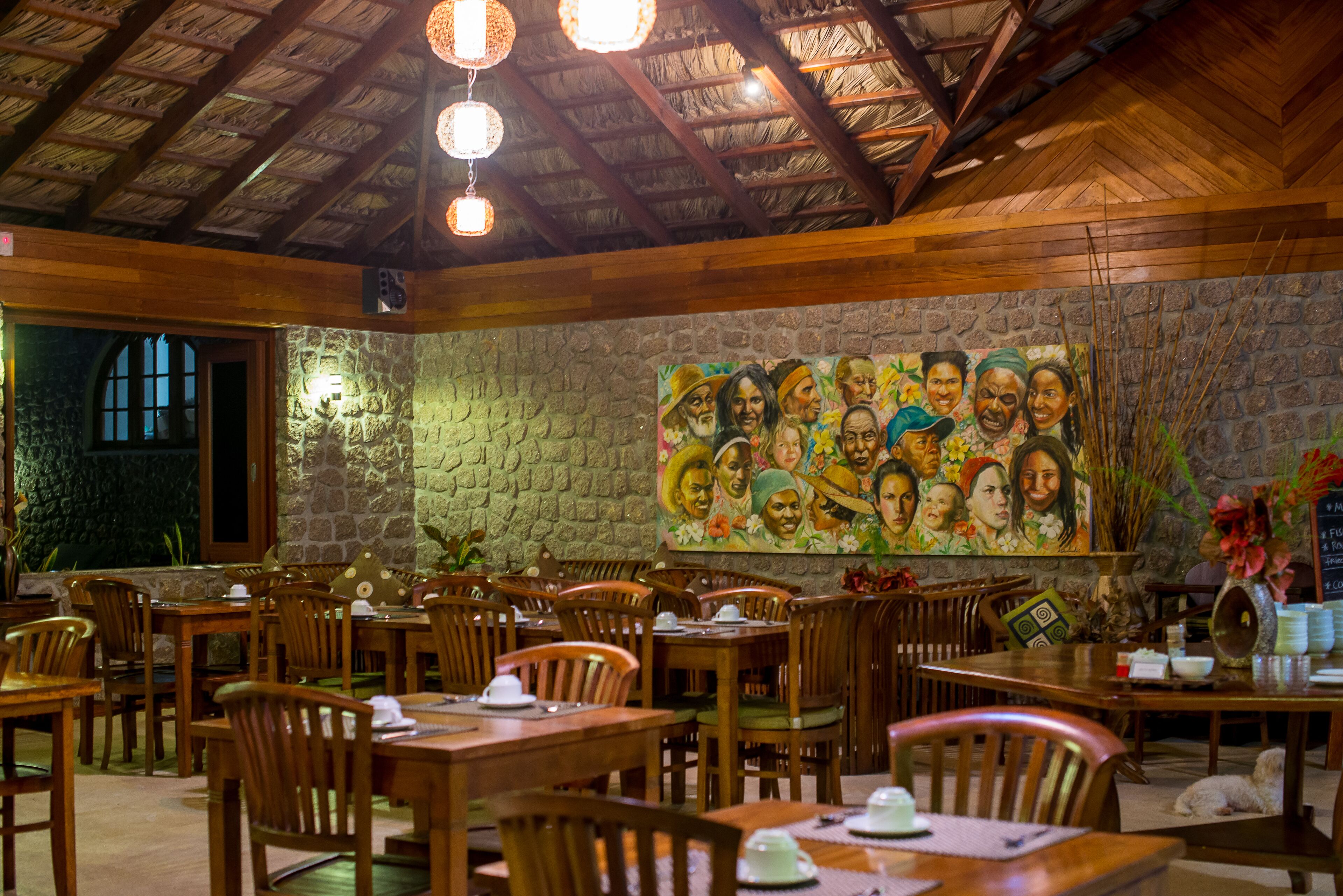 Un restaurante con mesas y sillas de madera, un muro de piedra y un mural con gente.