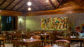Un restaurante con mesas y sillas de madera, un muro de piedra y un mural con gente.