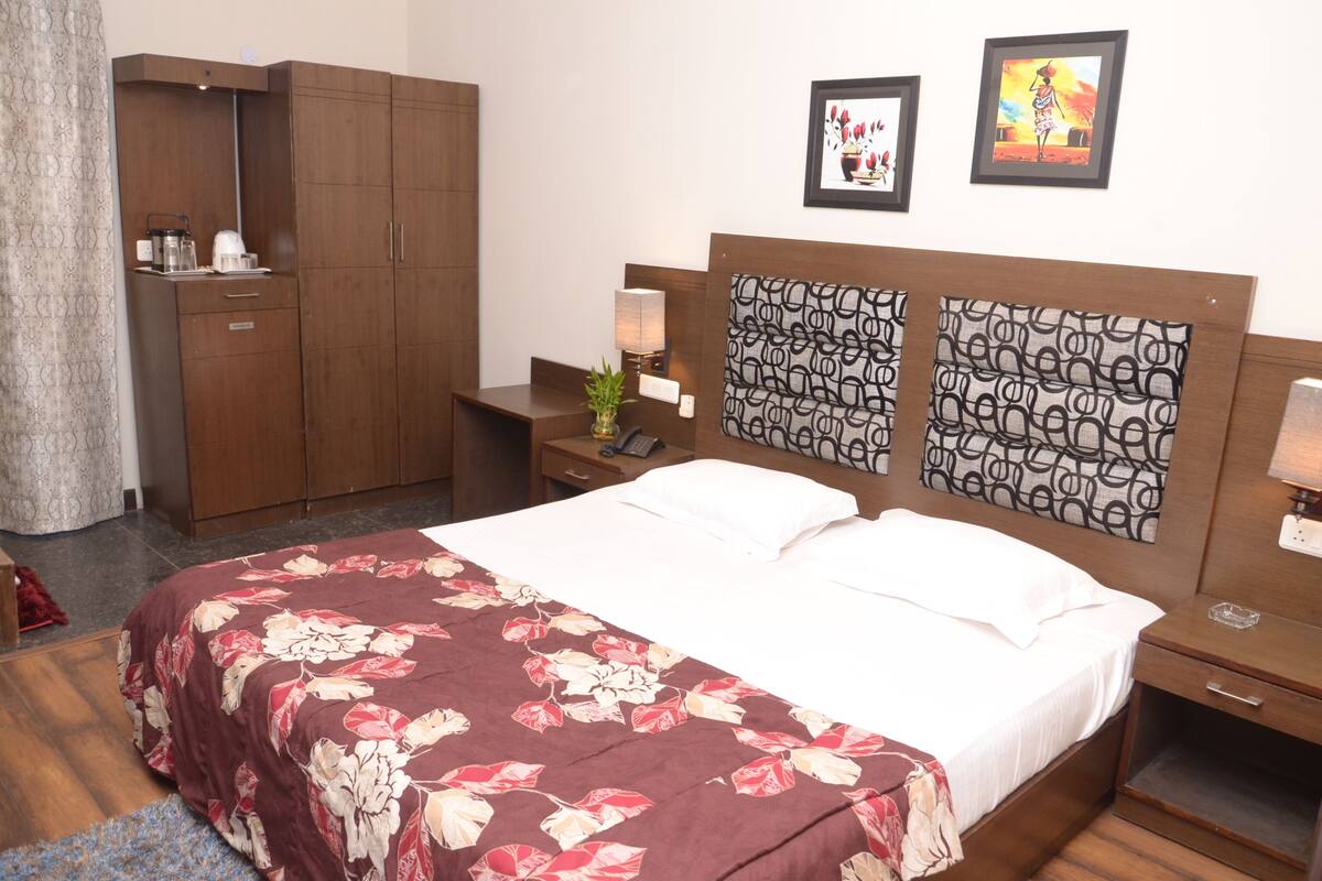 A hotel room with a large bed, a wardrobe, a nightstand with a lamp, and two framed pictures on the wall.