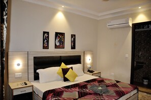 Une chambre d’hôtel comprenant un lit, des tables de chevet, un climatiseur fixé au mur et des œuvres d’art au-dessus du lit.