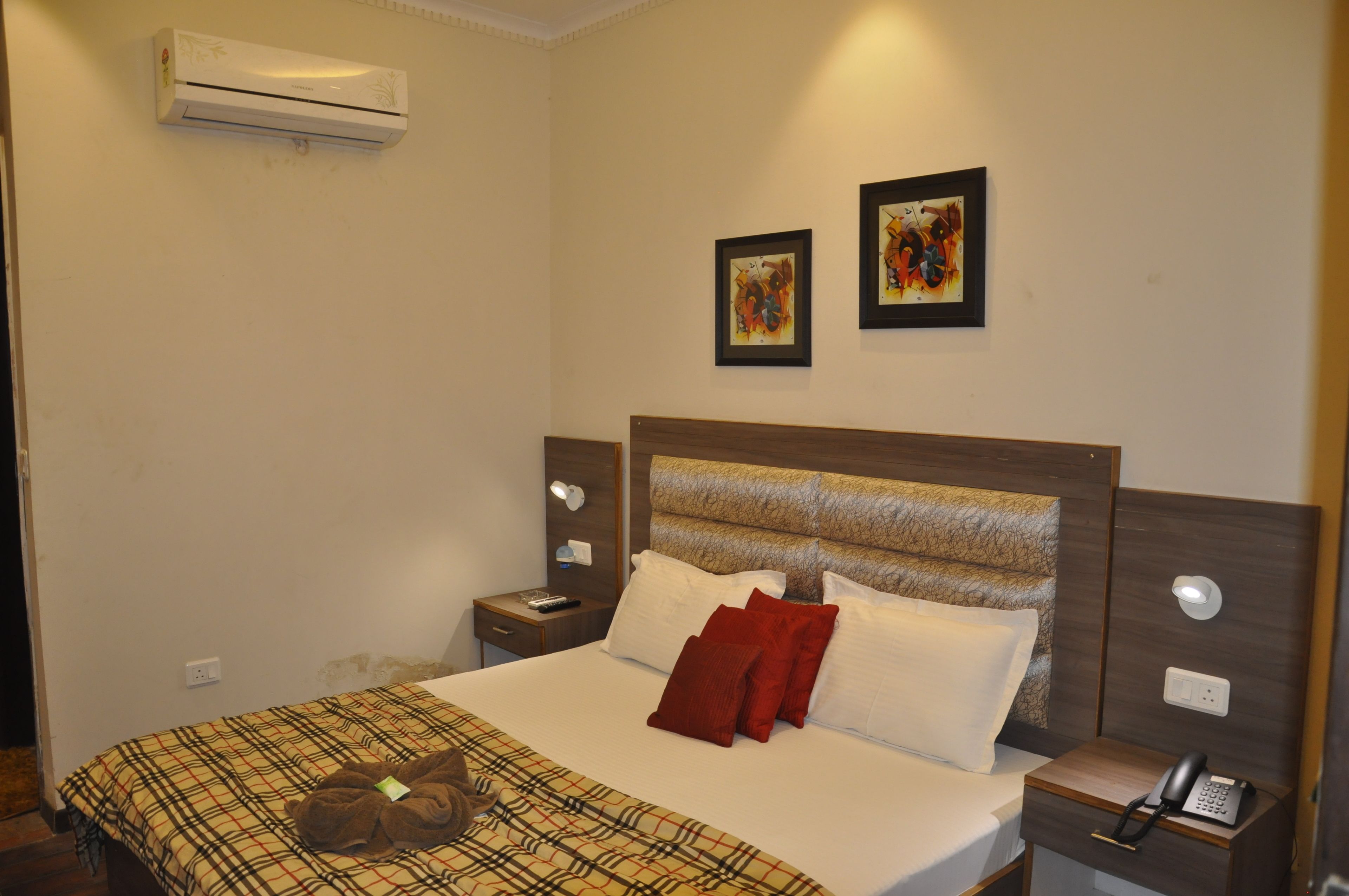 Habitación de hotel con cama, mesita de noche, teléfono y dos cuadros enmarcados en la pared.