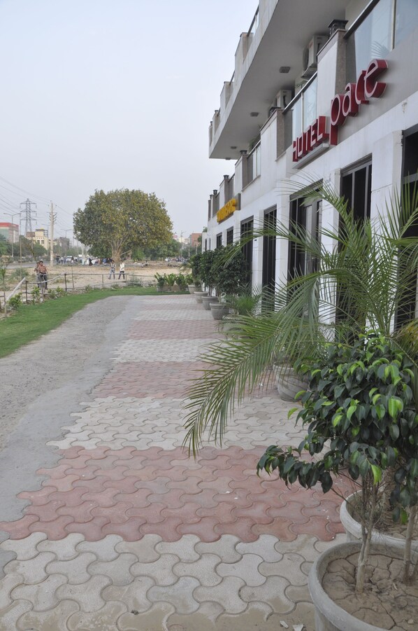 L’entrée d’un hôtel, avec un trottoir dallé, des plantes en pot et une vue dégagée sur la façade de l’immeuble.