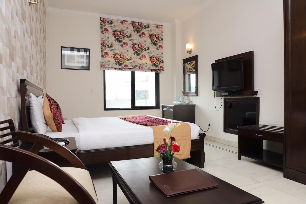 A hotel room with a bed, a desk, a chair, a TV, and a window with a floral blind.
