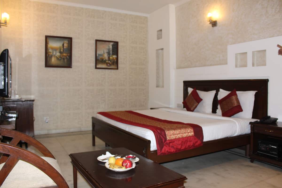 A hotel room with a bed, bedside table, and a small table with fruit. There are two paintings on the wall and a television on a stand.
