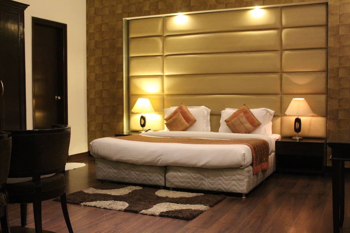 A hotel room with a large bed, two bedside tables with lamps, a dark wooden floor, and a brown patterned wall.