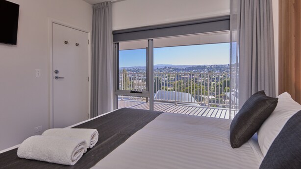 A hotel room with a large bed, a view of the city, and a balcony with a railing. - BIG4 Launceston Holiday Park (South Launceston)