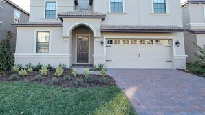 A two-story house with a garage, a front entrance with an arch, and a brick driveway. - ChampionsGate Platinum Resort Homes by Ocean Florida (Kissimmee)
