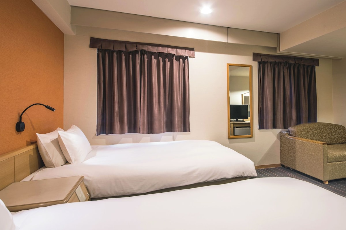 A hotel room with two beds, a sofa, a mirror, and a lamp.