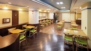 Un ristorante con tavoli di legno e sedie verdi, un bancone e quadri appesi al muro.