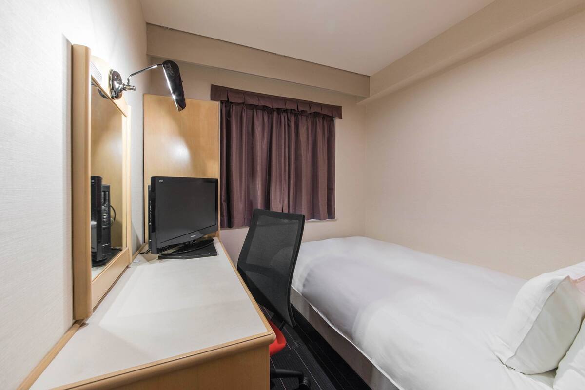 Una habitación de hotel con una cama, un escritorio con computadora, un televisor y un espejo.